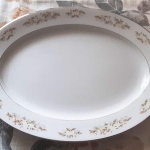 May include: Oval white serving platter with a gold floral pattern around the rim and a silver trim. The platter is empty and sits on a patterned surface.