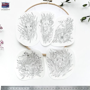 Könnte beinhalten: Fünf Schwarzweiß-Zeichnungen von australischen Tieren auf weißem Papier. Die Zeichnungen zeigen einen Koala, einen Vogel, einen Schnabeltier und zwei Kängurus. Die Zeichnungen sind auf weißem Hintergrund und von einem hölzernen Stickrahmen umgeben.