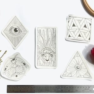 以下が含まれることがあります： 白い紙に描かれた5つの白黒の線画。絵には、蛾、目、鹿、幾何学模様、花が含まれています。