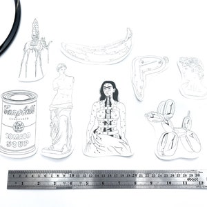 May include: A set of nine black and white line drawings of famous artworks, including a banana, a soup can, a balloon dog, and a sculpture of a woman. The drawings are printed on white paper and are arranged in a grid pattern.