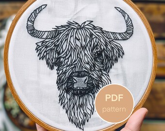 Puede incluir: Patrón de bordado en blanco y negro de la cabeza de una vaca de las tierras altas con pelo largo y peludo. El patrón está en un aro y dice "PDF pattern" en un círculo marrón.