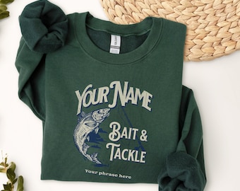 Op de afbeelding: Een donkergroen sweatshirt met een vintage-stijl afbeelding van een vis en een hengel. De tekst "YOUR NAME Bait & Tackle" is op het sweatshirt gedrukt. De zin "Your phrase here" is onder de afbeelding gedrukt.