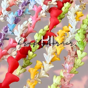 May include: A collection of multi-colored beaded strands featuring small flower-shaped beads in shades of red, yellow, green, pink, white, blue, and purple. The strands are arranged in a cluster, and the text kraftykorner is visible in the center.