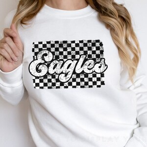May include: White sweatshirt with a black and white checkered design and the word "Eagles" in a retro font.