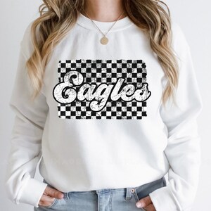 May include: White sweatshirt with a black and white checkered design and the word "Eagles" in a retro font.