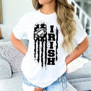 Puede incluir: Camiseta blanca con un gráfico en blanco y negro de una bandera estadounidense con un balón de fútbol y la palabra "IRISH" impresa en ella.