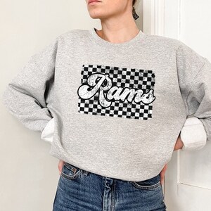 May include: A gray sweatshirt with a black and white checkered design and the word "Rams" in a retro font.