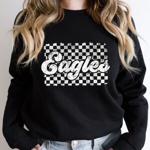 May include: Black sweatshirt with a white checkered pattern and the word "Eagles" in a retro font.
