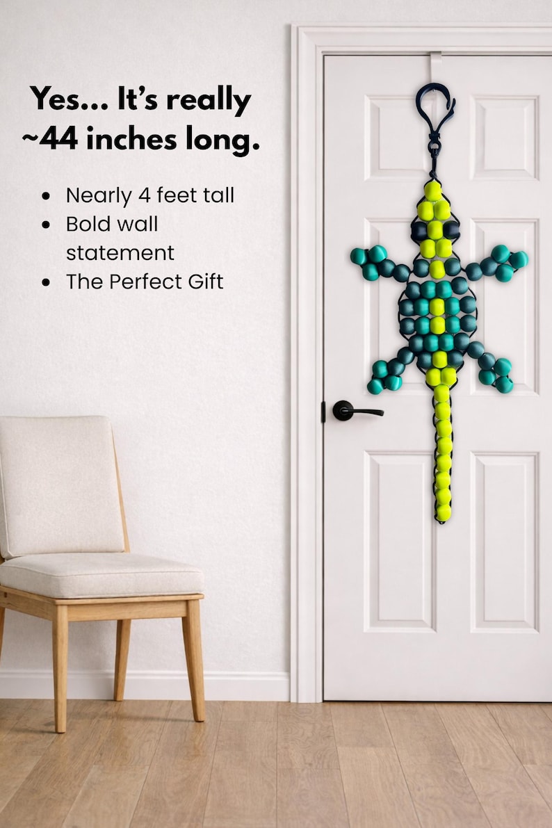 Puede incluir: Un adorno de pared con forma de lagarto hecho con cuentas, de aproximadamente 112 cm de largo, en tonos verdes, turquesas y amarillos, cuelga de una puerta blanca. El texto de la imagen dice "Yes... It's really ~44 inches long."