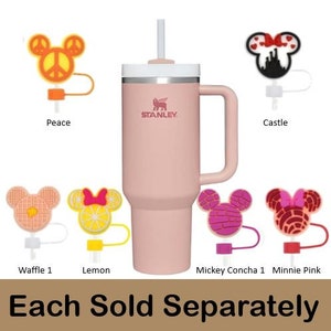May include: A pink Stanley brand travel mug with a handle and a variety of colorful silicone straw toppers. The toppers include a peace sign, a castle, a waffle, a lemon, a Mickey Mouse concha, and a Minnie Mouse with a pink bow. The text "Each Sold Separately" is printed below the image.