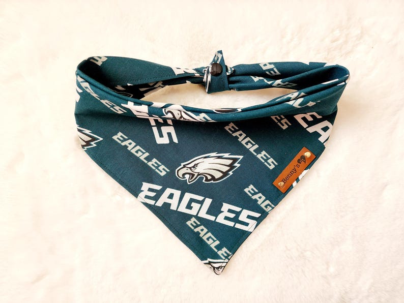 May include: Green and white dog bandana with a Philadelphia Eagles logo and the text "Eagles" repeated throughout. The bandana has a brown label with the text "Benny's" on it.