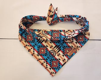 May include: A blue, red and brown patterned bandana with a dreamcatcher design. The bandana has a brown leather tag with the text "Penny's" on it.