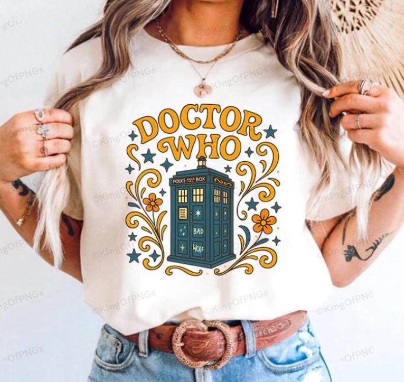 A woman wearing a white t-shirt with a graphic design featuring a blue telephone booth and decorative elements.