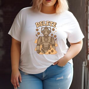 A woman wearing a white t-shirt with a graphic design of a robot character and the word "DELETE" printed on it.