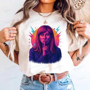 A woman wearing a white t-shirt with a colorful graphic of a woman with long hair and a hand covering her mouth.