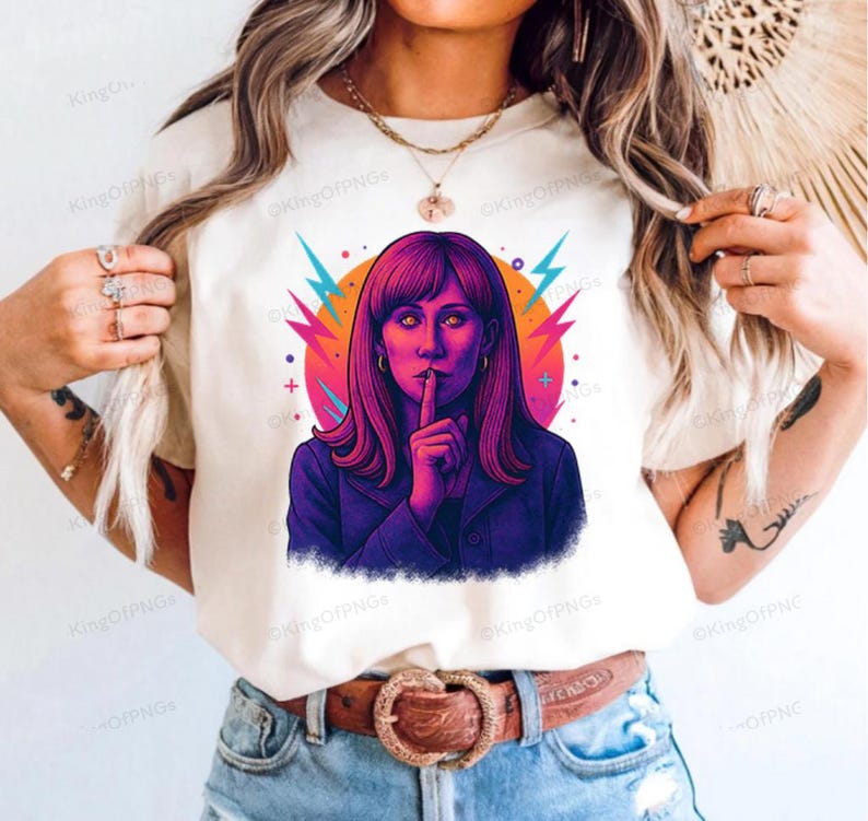 A woman wearing a white t-shirt with a colorful graphic of a woman with long hair and a hand covering her mouth.