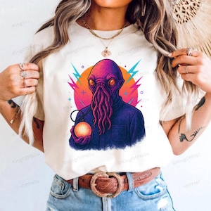 A person wearing a white t-shirt with a colorful graphic of an alien-like creature holding a glowing orb.