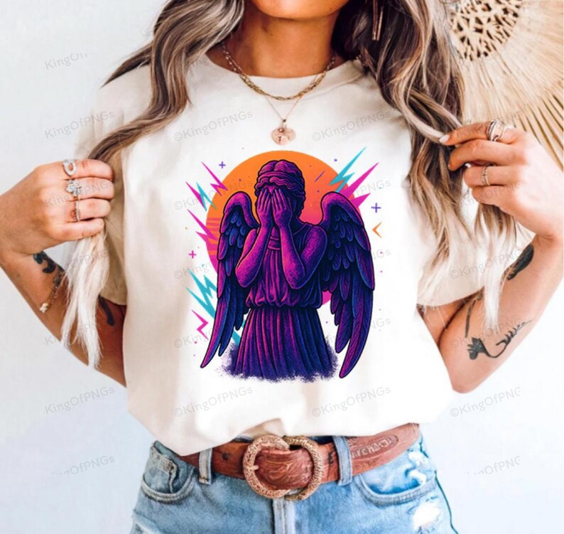 A woman wearing a white t-shirt with a graphic design of a purple angel with wings and a face covering her mouth.