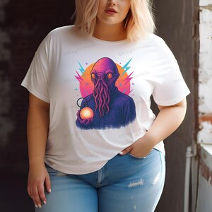 A woman wearing a white t-shirt with a colorful graphic of an alien-like creature holding a glowing orb.