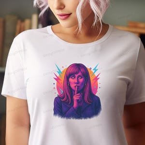 A woman with long hair wearing a white t-shirt with a colorful graphic of a woman making a hand gesture.