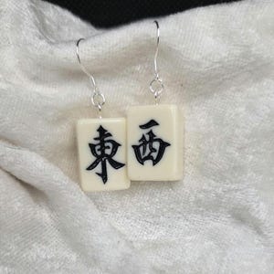 以下が含まれることがあります： クリーム色の長方形のタイルに黒い漢字が描かれたイヤリングのペア。イヤリングには銀色のフックが付いています。タイルは滑らかで光沢のある素材で作られている可能性があります。
