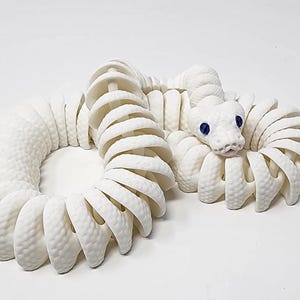 May include: A white, articulated snake sculpture with a textured body and a detailed head. The snake's eyes are blue. The sculpture is coiled in a circular shape, showcasing its segmented design.