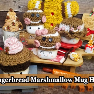 May include: Handmade crochet mug toppers resembling gingerbread men, cupcakes, and a Christmas tree. The toppers are brown, white, and pink, with button and bow details. The text "Gingerbread Marshmallow Mug Hats" is displayed at the bottom.