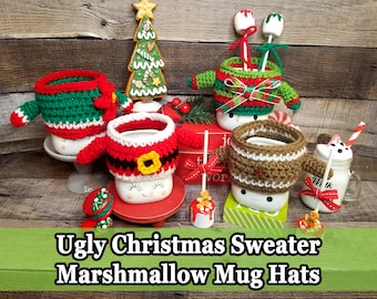 Puede incluir: Una colección de fundas para tazas hechas a mano, tejidas a ganchillo, diseñadas para parecerse a feos suéteres navideños. Las fundas son de varios colores, incluyendo rojo, verde y marrón, y se colocan en tazas. La imagen también incluye un árbol de pan de jengibre y golosinas de malvavisco. El texto en la imagen dice "Ugly Christmas Sweater Marshmallow Mug Hats."
