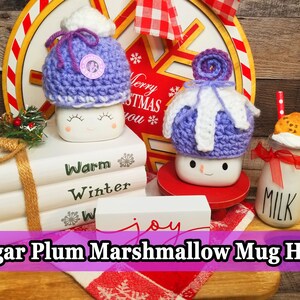 May include: Handmade Sugar Plum Marshmallow Mug Hats. The image shows two marshmallow mugs with crocheted hats in purple and white. One mug has a hat with a pom-pom, and the other has a swirl design. A milk bottle with a cookie and a red straw is also visible.