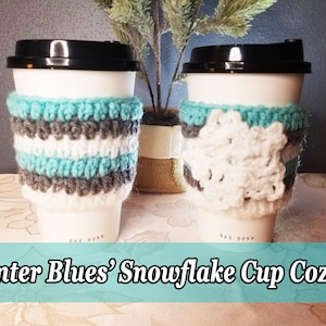 May include: Two white coffee cups with crocheted cup cozies. One cozy is striped in white, grey, and teal. The other cozy is white with a snowflake design. The text 'Rae Dunn' is visible on the bottom of each cup. The text 'Winter Blues' Snowflake Cup Cozies' is visible at the bottom of the image.