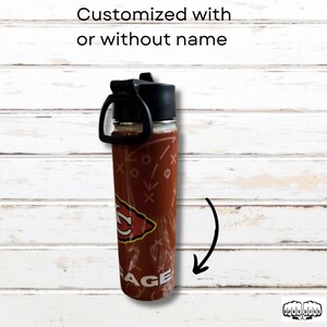 May include: A clear water bottle with a black lid and handle. The bottle is decorated with a football play design and a team logo. The text "AGE" is visible on the bottom of the bottle. The text "Customized with or without name" is at the top.