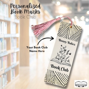 May include: A white bookmark with a black and white illustration of an open book with flowers and butterflies. The bookmark has a pink tassel and the text "Boozy Babes Book Club" on it.