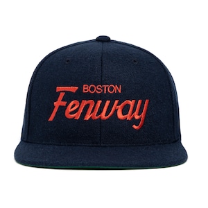 Puede incluir: Una gorra de béisbol azul marino con un logotipo bordado en rojo que dice "BOSTON Fenway".
