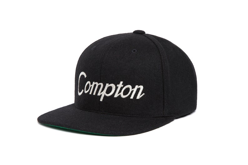 Peut inclure: Une casquette de baseball en laine noire avec un logo "Compton" brod&eacute; en blanc.