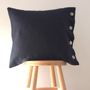 May include: A dark blue linen pillow with four white buttons down the side. The pillow is sitting on a wooden stool.