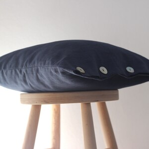May include: A dark blue linen pillow with three decorative buttons. The pillow is sitting on a wooden stool.