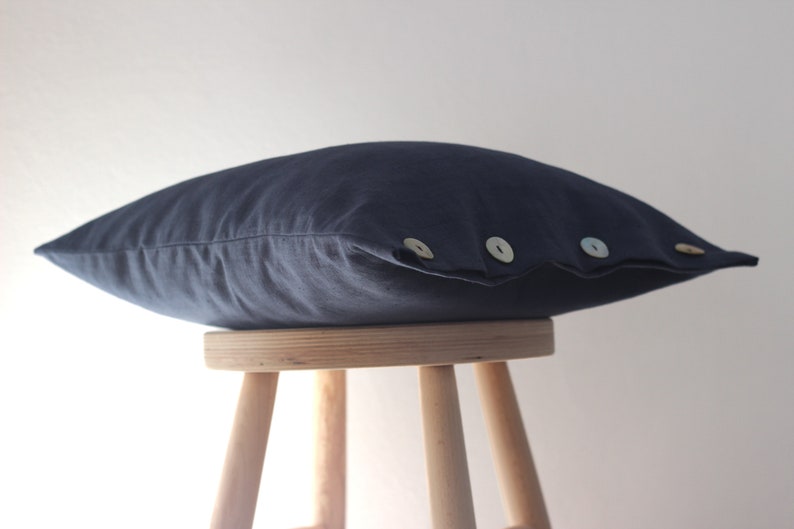 May include: A dark blue linen pillow with three decorative buttons. The pillow is sitting on a wooden stool.