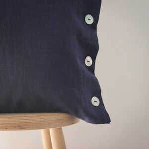 May include: A dark blue linen pillow with three white buttons on the side.