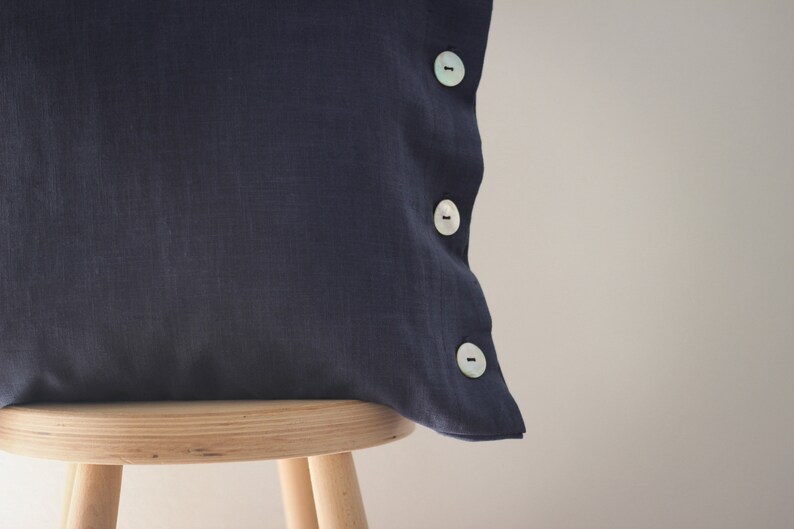 May include: A dark blue linen pillow with three white buttons on the side.