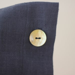 May include: A dark blue linen pillow cover with a large, round, cream-colored button.