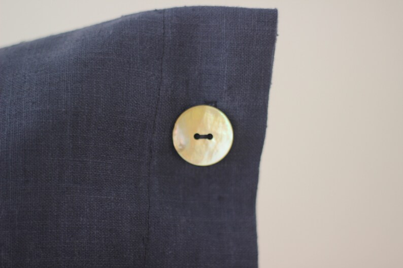 May include: A dark blue linen pillow cover with a large, round, cream-colored button.