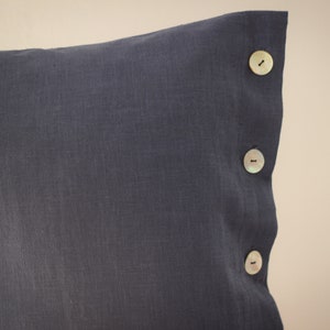 May include: A dark gray linen pillow with three white buttons on the side.