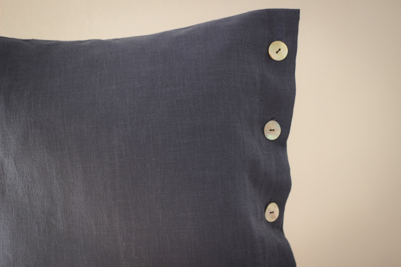May include: A dark gray linen pillow with three white buttons on the side.