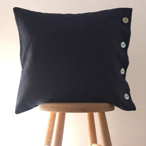 May include: A dark blue pillow with four decorative buttons on the side. The pillow is sitting on a wooden stool.