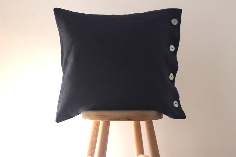 May include: A dark blue pillow with four decorative buttons on the side. The pillow is sitting on a wooden stool.