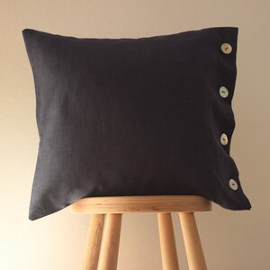 May include: A dark blue pillow with four light colored buttons down the side. The pillow is sitting on a wooden stool.