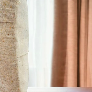 May include: A beige and white throw pillow with a tassel detail. The pillow is made of a textured fabric and has a subtle speckled pattern.