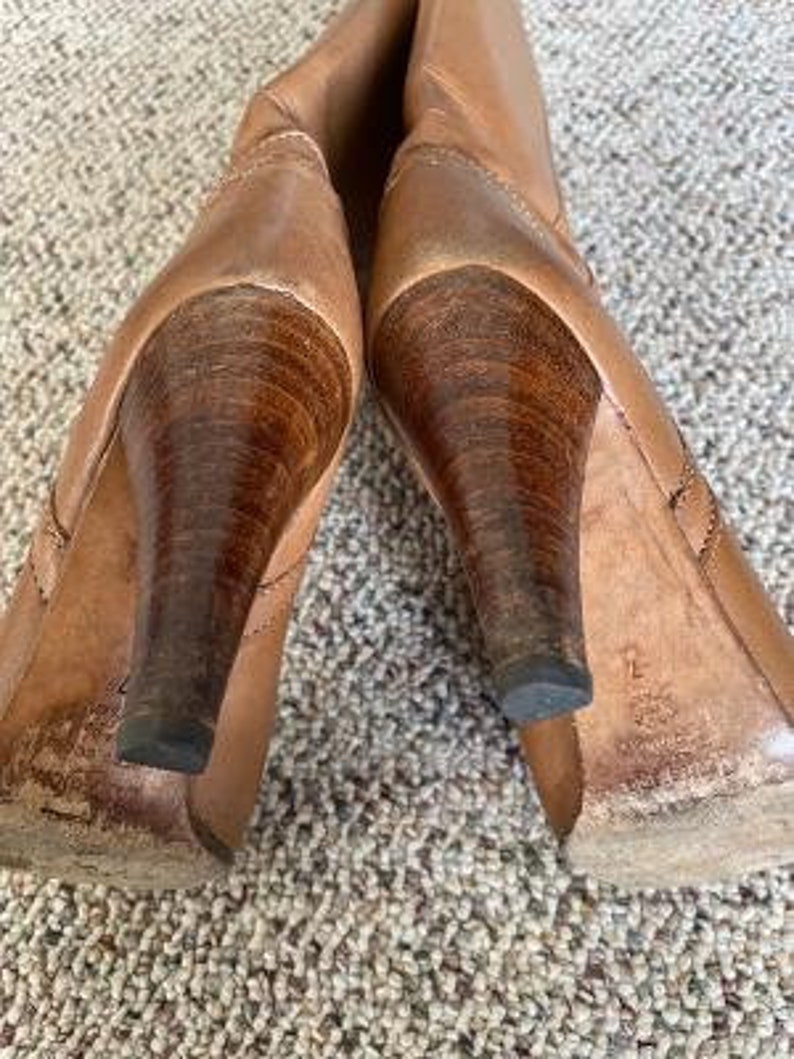Puede incluir: Un par de botas de tac&oacute;n de cuero marr&oacute;n con punta puntiaguda. Las botas tienen un tac&oacute;n de madera y un eje de cuero marr&oacute;n.