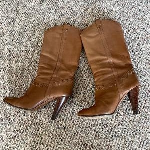 Puede incluir: Un par de botas de cuero marr&oacute;n de ca&ntilde;a alta con punta puntiaguda y tac&oacute;n de bloque.