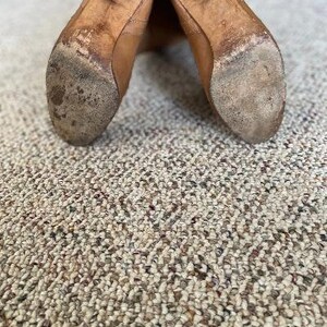 Puede incluir: Un par de botas de cuero marr&oacute;n con punta puntiaguda y tac&oacute;n bajo. Las botas est&aacute;n gastadas y tienen un aspecto desgastado.